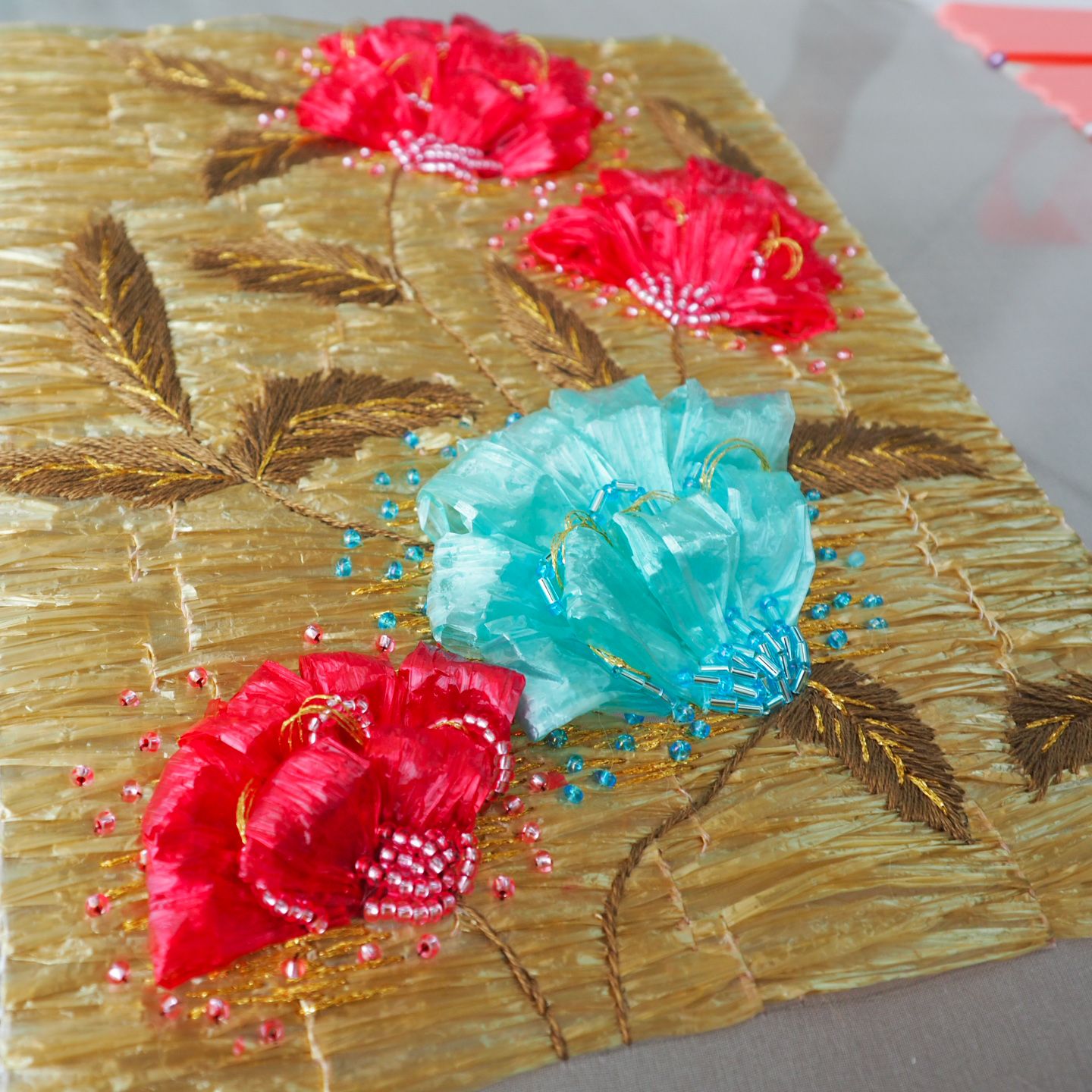 Givenchy 1962 Raffia Couture Embroidery Study — Floral Motif Couture embroidery sample inspired by a 1962 Givenchy evening dress, featuring a raffia base with sculpted red and turquoise flowers, gold thread leaves, and bead details