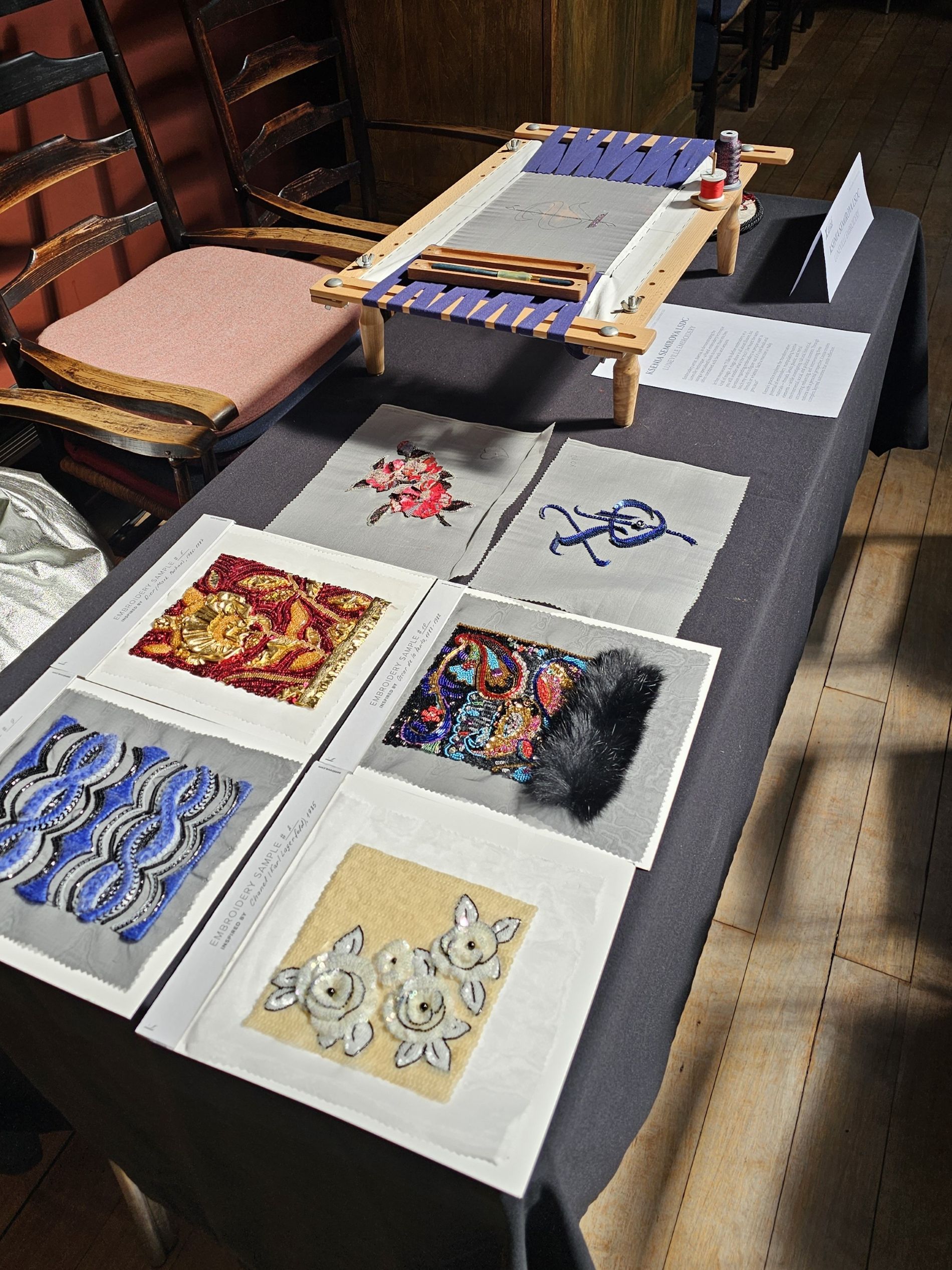 Luneville Embroidery Demonstration with Couture Samples – May 2025 Luneville embroidery demonstration setup with a wooden frame, hooks, threads, and several couture-inspired embroidery samples displayed on a table during the Society of Designer Craftsmen meeting in May 2025.