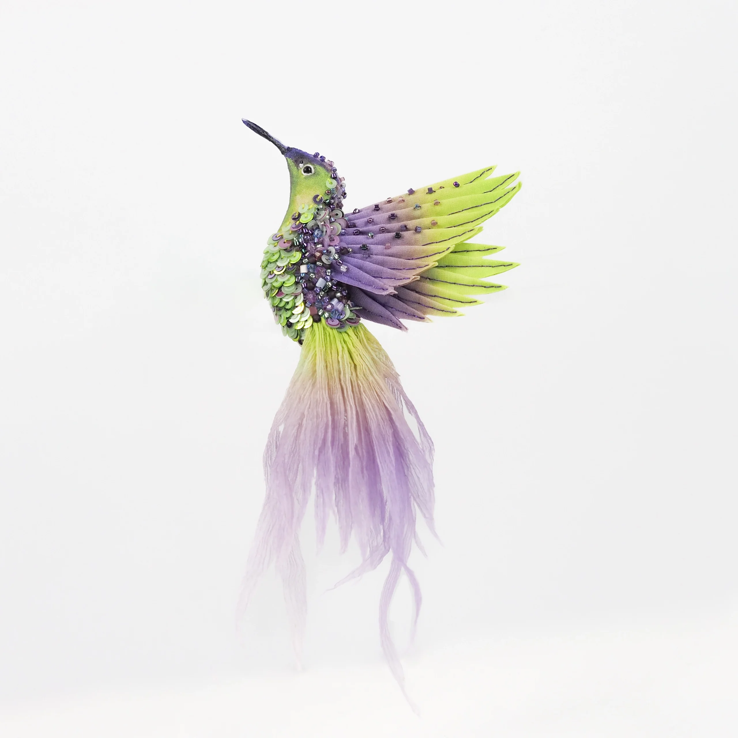 A luxury handcrafted brooch featuring a vibrant lime green and purple hummingbird design with intricate feather details and a flowing gradient tail. This unique wearable art piece blends bold colors and delicate craftsmanship, perfect for adding an elegant touch to any outfit or as a Gift for Nature Lovers