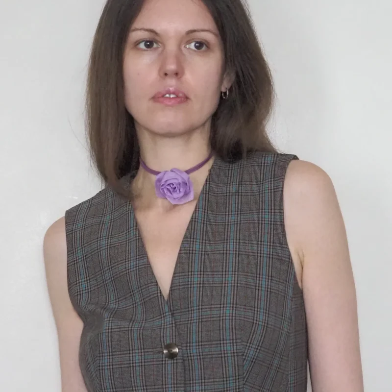 Handmade lavender silk rose choker worn by a woman in a tailored plaid vest. This elegant yet minimalist choker features a delicate rose crafted from silk chiffon, adding a subtle touch of floral charm to both everyday and special occasions. The rose measures approximately 9 cm in diameter and is secured with a soft suede cord and toggle clasp. Perfect for eveningwear, gothic styles, or as a statement accessory