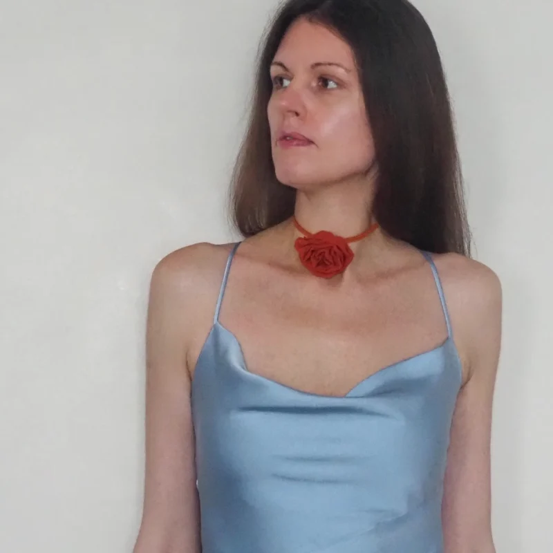 Model wearing a handmade red silk rose choker, featuring a delicate rose design on a suede cord, paired with a light blue satin dress for an elegant look