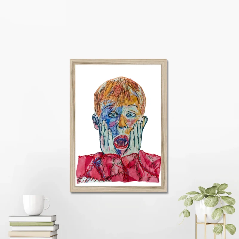 Framed Home Alone Kevin embroidery art poster featuring a colorful abstract depiction of Kevin's iconic surprised expression, displayed on a white wall with minimalist decor, including stacked books and a small potted plant | Christmas Movie Wall Art Print