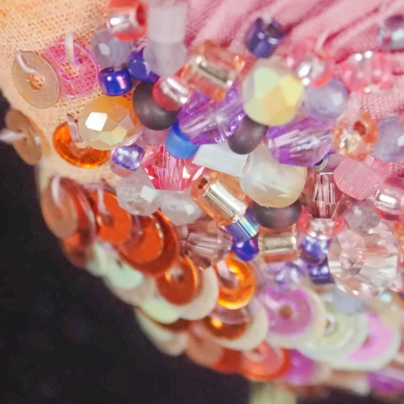 Close-up detail of the intricate beadwork on the Flying Hummingbird Brooch, featuring a variety of colorful beads and sequins in shades of pink, orange, purple, and translucent hues.