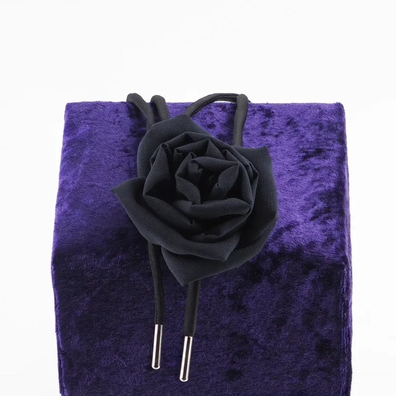 Handcrafted black silk rose choker by Ksenia Semirova, featuring a delicate silk rose centerpiece and adjustable black satin lace with nickel-free metal ends, displayed on a luxurious purple backdrop. Perfect for elegant styling and timeless craftsmanship.