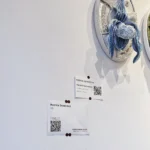 Hand-embroidered artwork titled 'Lady Slipper Blue and White' by Ksenia Semirova, displayed on a gallery wall with tags featuring the artist's name and pricing information