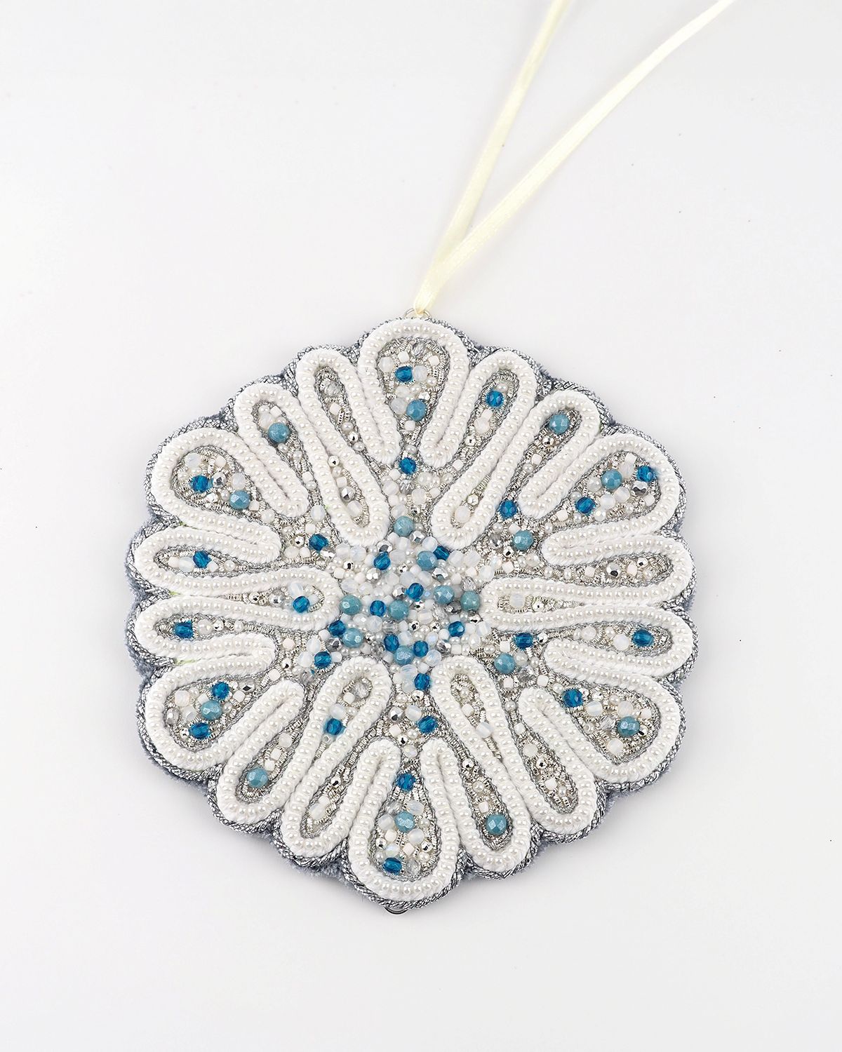 Circular snowflake ornament from the Jewels of Winter series by Ksenia Semirova, hand-embroidered with pearl-setting technique using white, silver, and blue beads.