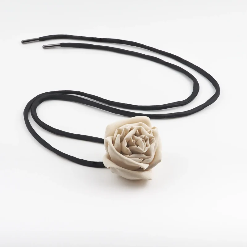 Image of a handmade nude silk rose choker with a detailed nude silk rose centerpiece and adjustable black satin lace, laid flat for display. Perfect for versatile styling and elegant outfits