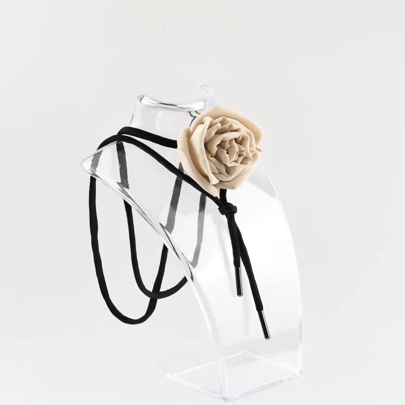 Nude silk rose choker by Ksenia Semirova displayed on a clear acrylic stand. This handcrafted accessory features a nude silk rose centerpiece, black satin lace, and nickel-free metal ends, highlighting elegant design and artisanal craftsmanship.