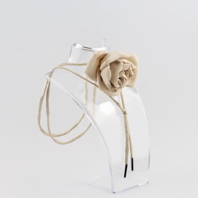 Nude silk rose choker by Ksenia Semirova displayed on a clear acrylic stand. This handcrafted accessory features a nude rose centerpiece, nude dupioni silk lace, and nickel-free metal ends, highlighting elegant design and artisanal craftsmanship.