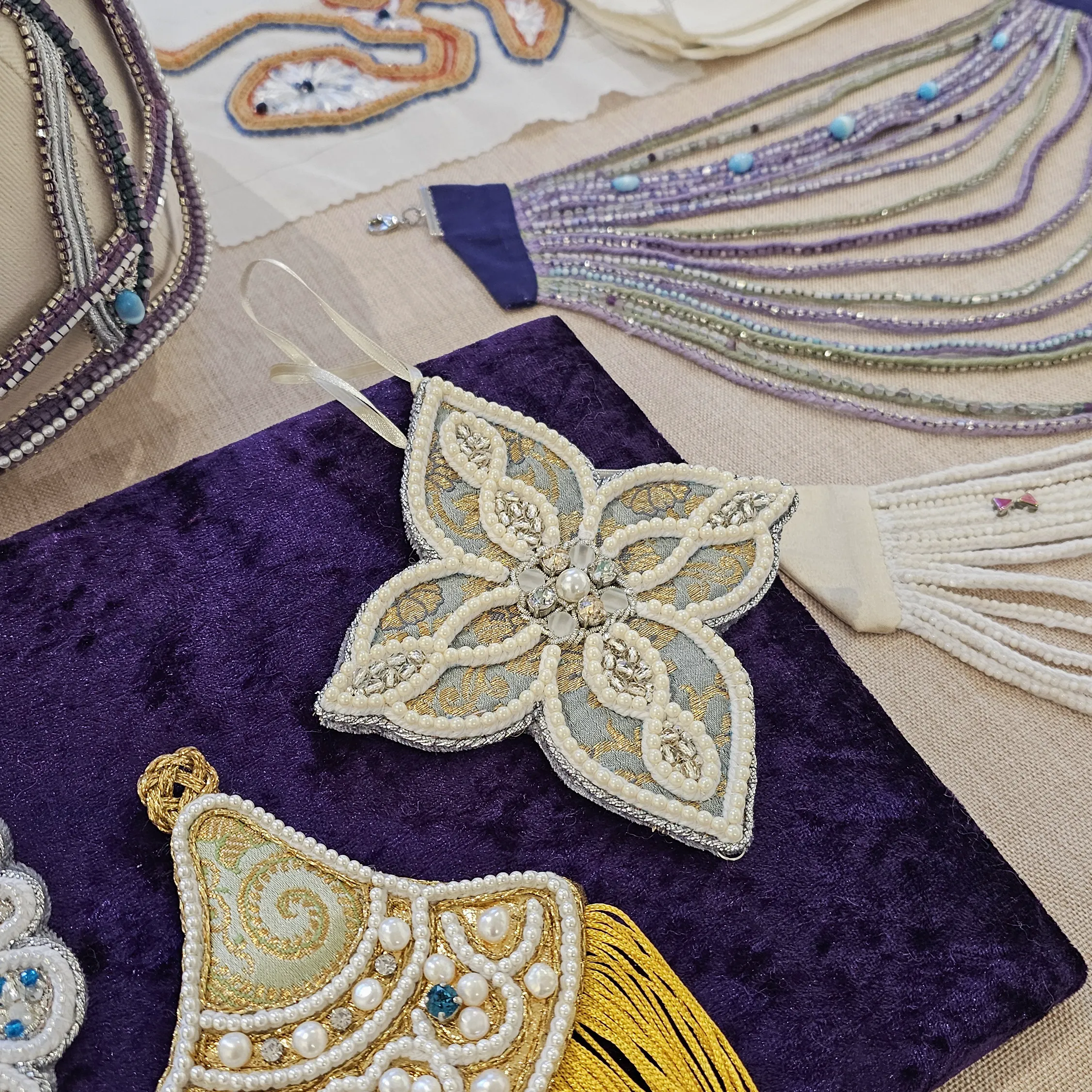 Pearl Embroidery Demonstration at SoShiro Gallery | Ksenia Semirova. Embroidery art Collection of intricate pearl embroidery samples displayed on a table, featuring gold and silver designs with detailed beadwork and tassels