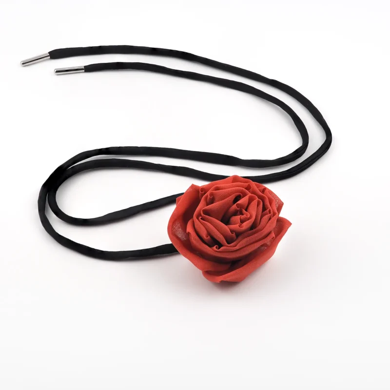 Image of a handmade red silk rose choker with a detailed red silk rose centerpiece and adjustable black satin lace, laid flat for display. Perfect for versatile styling and elegant outfits