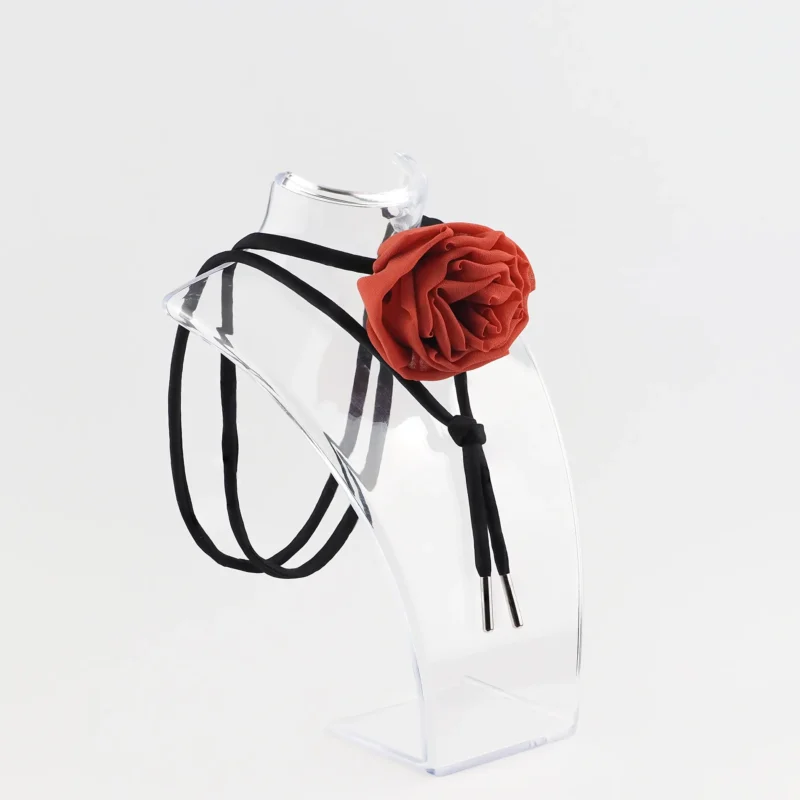 Red silk rose choker by Ksenia Semirova displayed on a clear acrylic stand. This handcrafted accessory features a red silk rose centerpiece, black satin lace, and nickel-free metal ends, highlighting elegant design and artisanal craftsmanship.