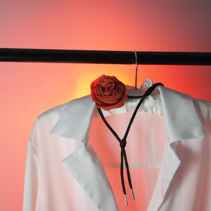 A handcrafted red silk rose choker with a black satin cord, displayed on a white shirt against a vibrant gradient background. Perfect for gothic and elegant styles