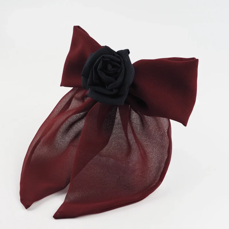 A burgundy chiffon bow hair accessory featuring a handcrafted black silk rose at the center. The design combines soft, flowing chiffon with a bold centerpiece, attached to a metal hair clip for a dramatic and elegant hairstyle addition.