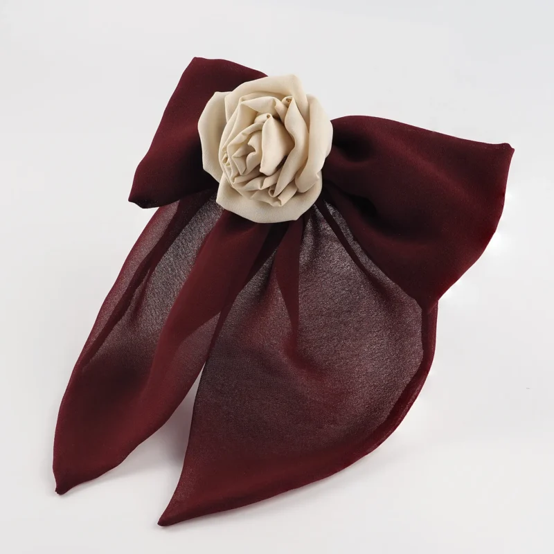 A burgundy chiffon bow hair accessory featuring a handcrafted cream-colored silk rose at the center. The elegant bow is structured for a flowing appearance and is attached to a metal hair clip, ideal for adding a sophisticated touch to any hairstyle