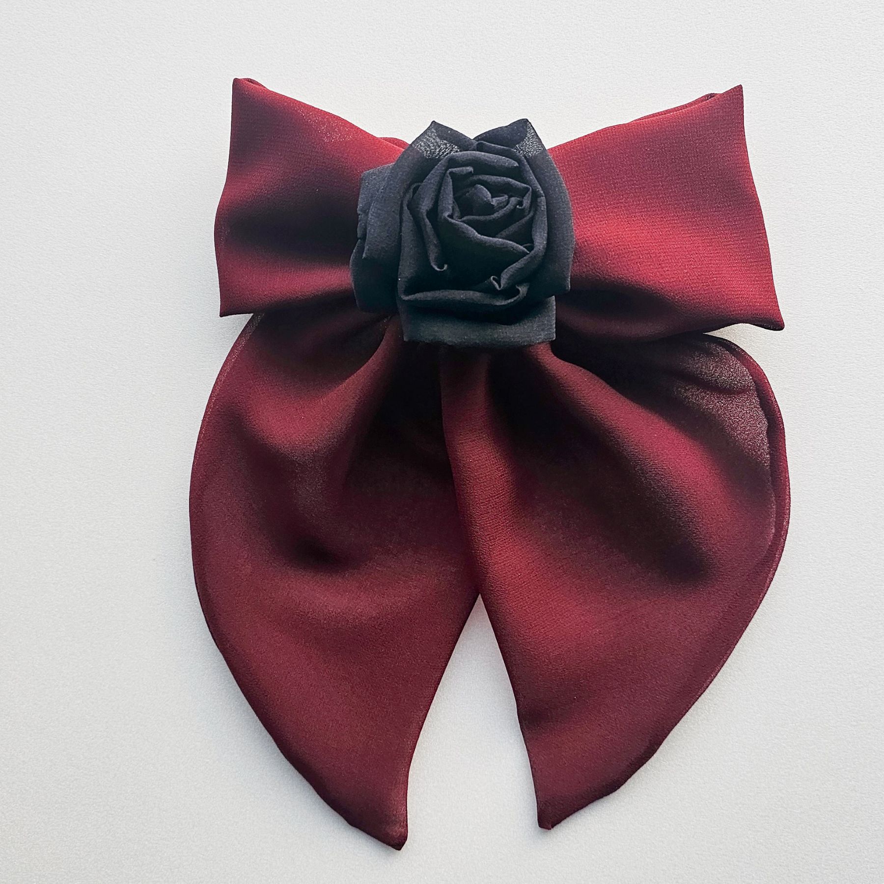 Handmade maroon chiffon bow hair clip featuring a large, elegant bow with soft flowing tails and adorned with a black silk rose at the center. Perfect for gothic and romantic styles