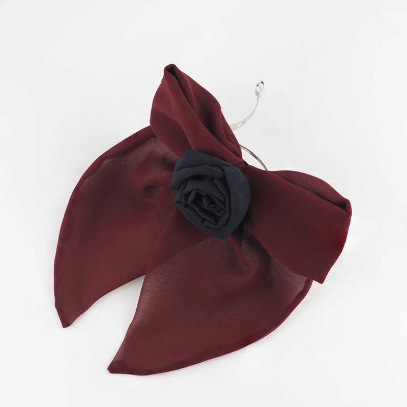 A handcrafted burgundy chiffon bow hair accessory with a black silk rose at the center, featuring a structured yet delicate design. The bow is attached to a metal hair clip, making it a bold and elegant choice for styling