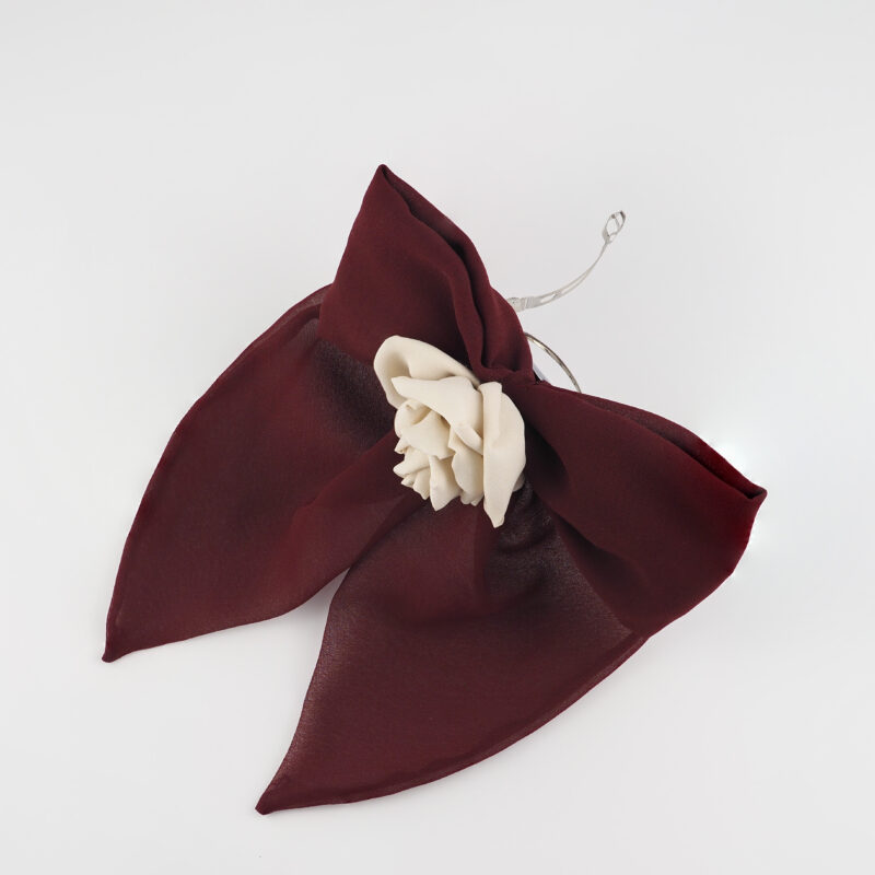 A handcrafted burgundy chiffon bow hair accessory featuring a cream-colored silk rose at the center. The bow has a soft, elegant design and is attached to a metal hair clip, perfect for creating a refined and unique look