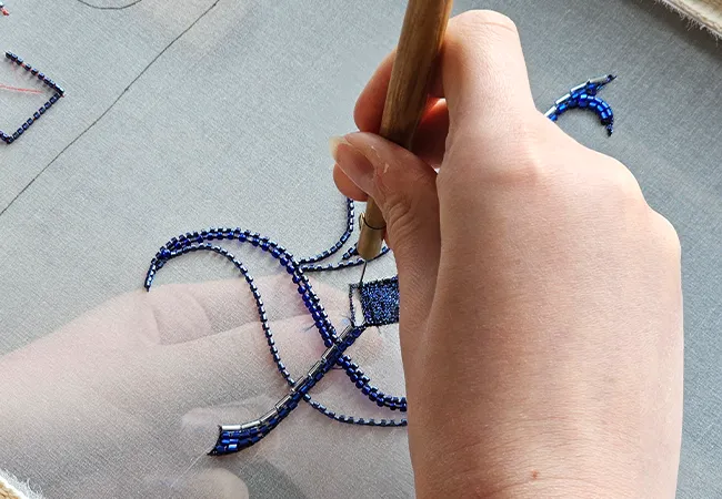 Beaded Luneville Embroidery Blue Glass Beads with Tambour Hook | Ksenia Semirova. Embroidery art Hand using a Luneville hook to embroider a curved design with blue seed beads and bugle beads on sheer fabric.