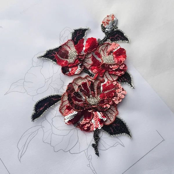 Red and black Luneville embroidery flower with sequins and beads on fabric, placed over a printed embroidery pattern.