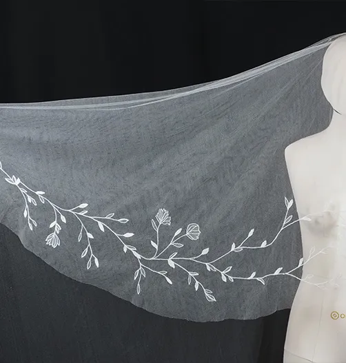 Close-up of hand-embroidered floral hem detail on a bespoke wedding veil, displayed on mannequin.