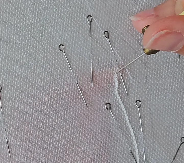 Tambour lace embroidery in progress, with the artist stitching white thread onto tulle using a tambour hook.