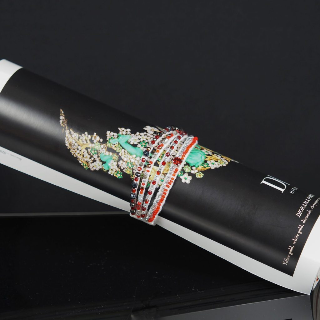 Handmade multi-strand bracelet in red, white, and black beads, created using pearl setting embroidery, displayed on a rolled magazine with floral artwork.