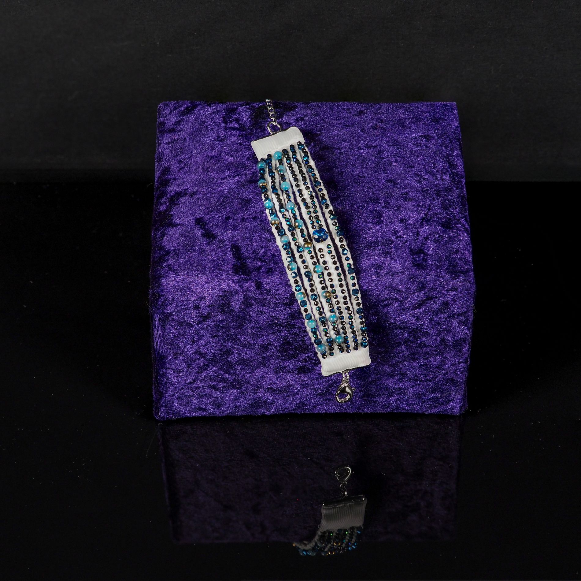 Finished Multi-Strand Beaded Bracelet Workshop Outcome | Ksenia Semirova. Embroidery art A completed multi-strand beaded bracelet in blue and black tones displayed on a purple velvet stand, showing the outcome of Ksenia Semirova’s offline workshop.