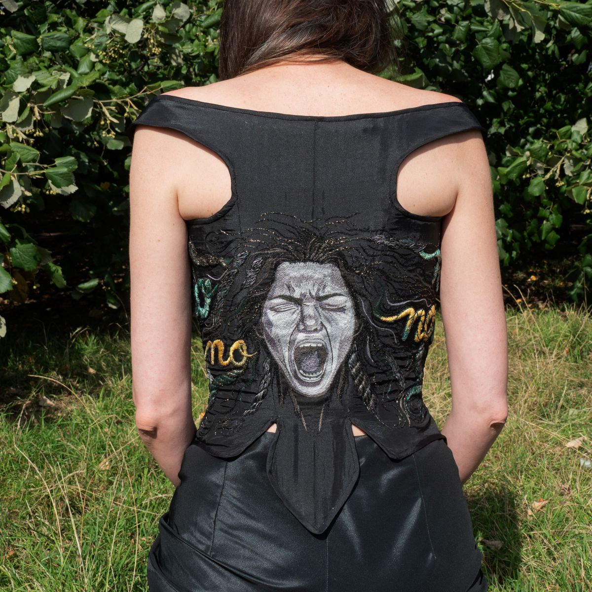 Close-up of hand embroidery showing screaming face, rope-like hair, and stitched “No” words on back of corset by Ksenia Semirova