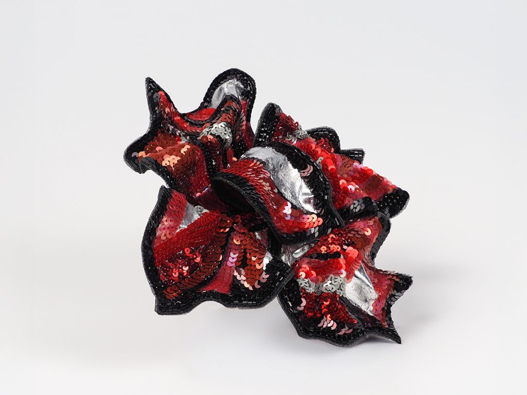Angled front view of red and black hand embroidered floral brooch by Ksenia Semirova, featuring silk organza petals with Italian sequins and silver highlights.