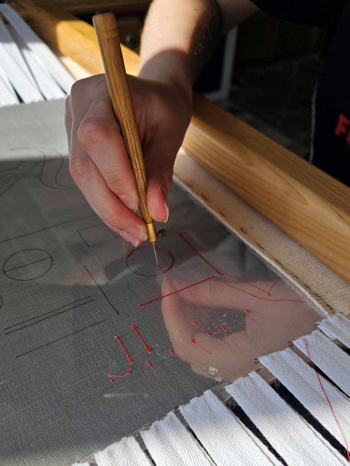 Luneville embroidery practice on sheer fabric showing tambour chain stitch in red thread, with simple lines, circles, and early letterforms stretched on a wooden embroidery frame.