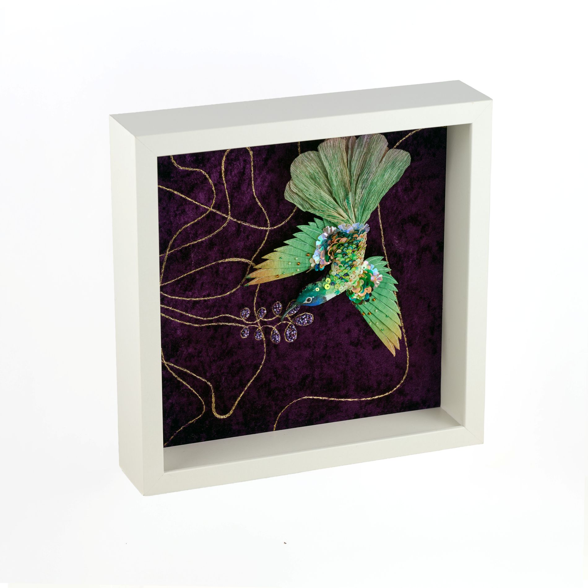 Angled view of framed textile wall art showing a three-dimensional silk hummingbird on a velvet background with hand-embroidered tropical floral motifs, Avian Oasis series.