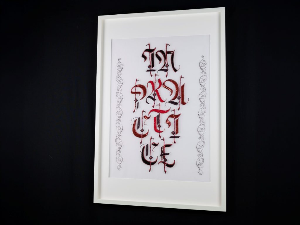 In Practice Framed Luneville Embroidery Artwork Angled view of In Practice, a framed gothic lettering artwork made in Luneville embroidery.