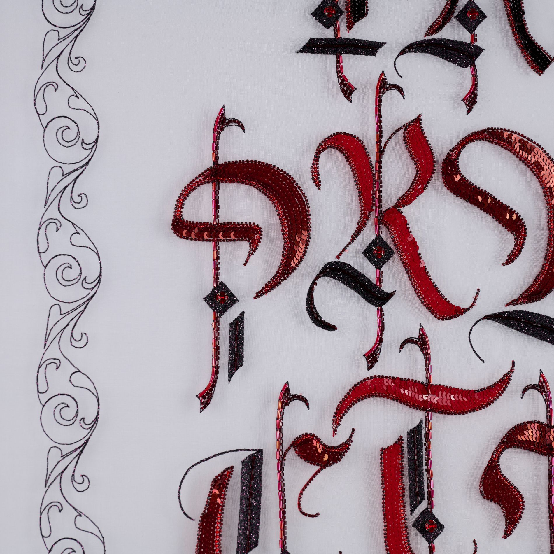 In Practice Luneville Embroidery Detail with Ornament Close-up of In Practice showing red and black embroidered gothic lettering with drawn ornamental border on the left.