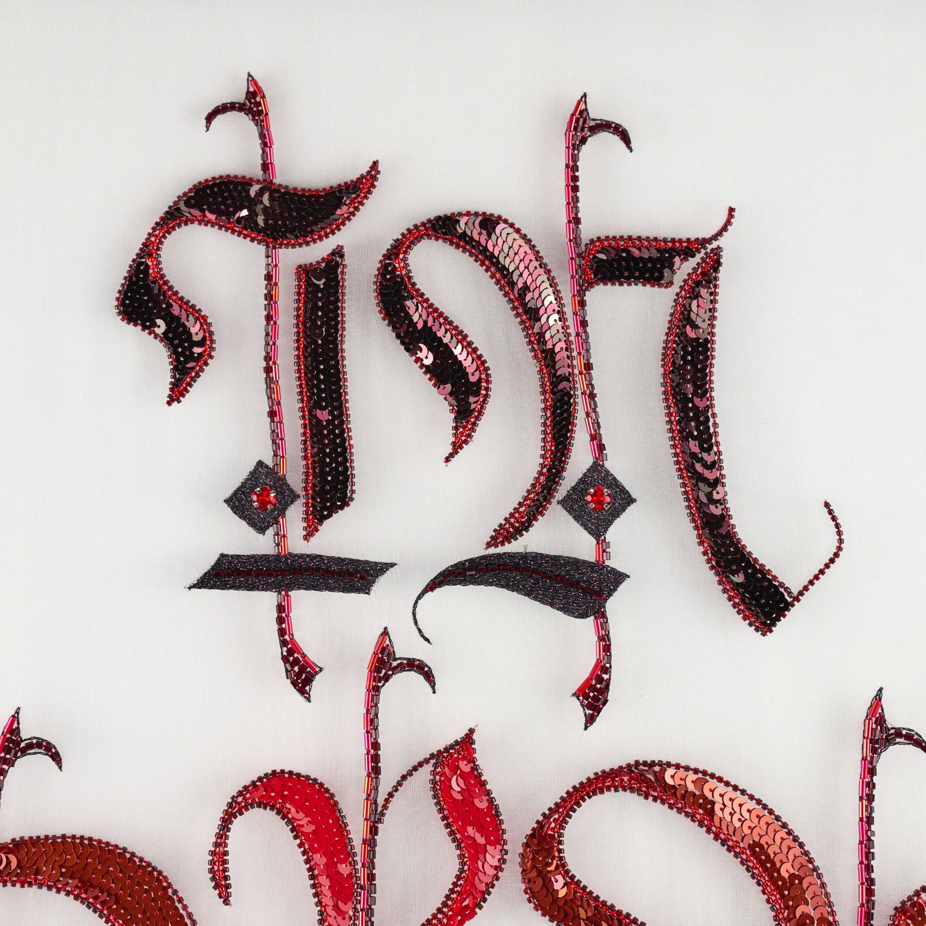 In Practice Upper Detail in Luneville Embroidery Close-up of the upper section of In Practice, showing black and red gothic letterforms in Luneville embroidery.