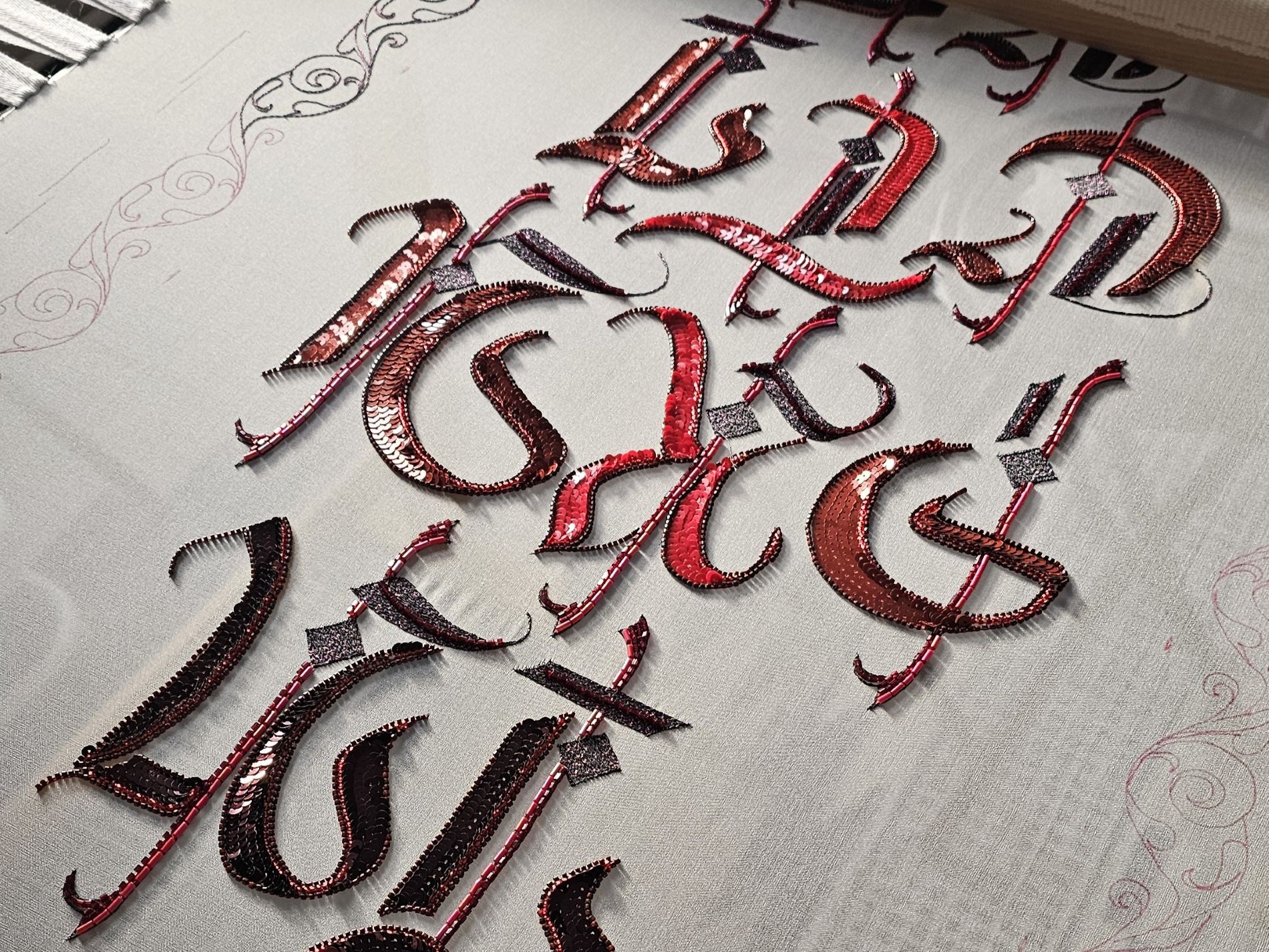 In Practice Work in Progress on Embroidery Frame Work in progress view of In Practice on an embroidery frame, showing red and black gothic lettering being developed in Luneville embroidery.