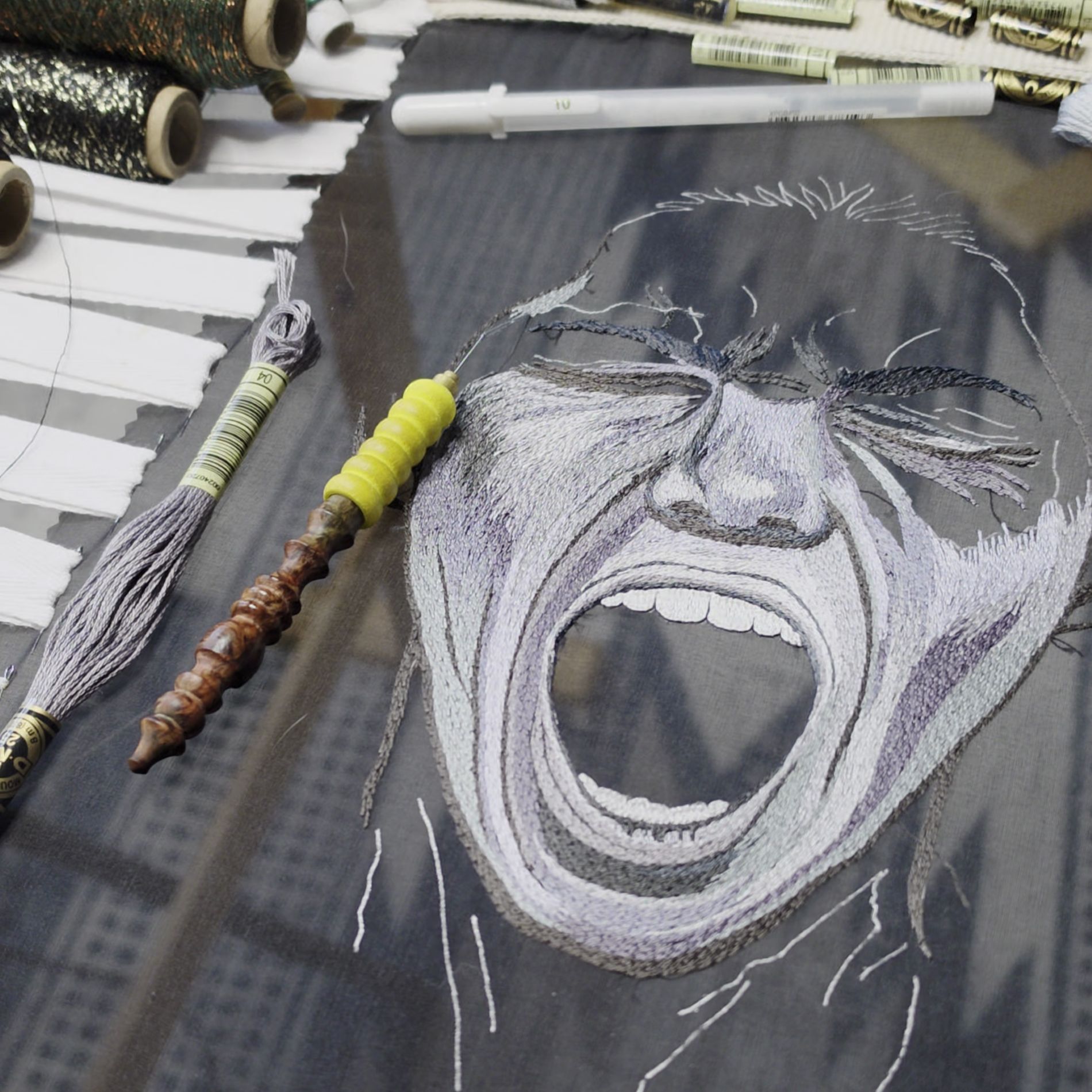 Studio progress image of Despair from the Power of No series, showing a hand embroidered screaming face with threads and embroidery tools.