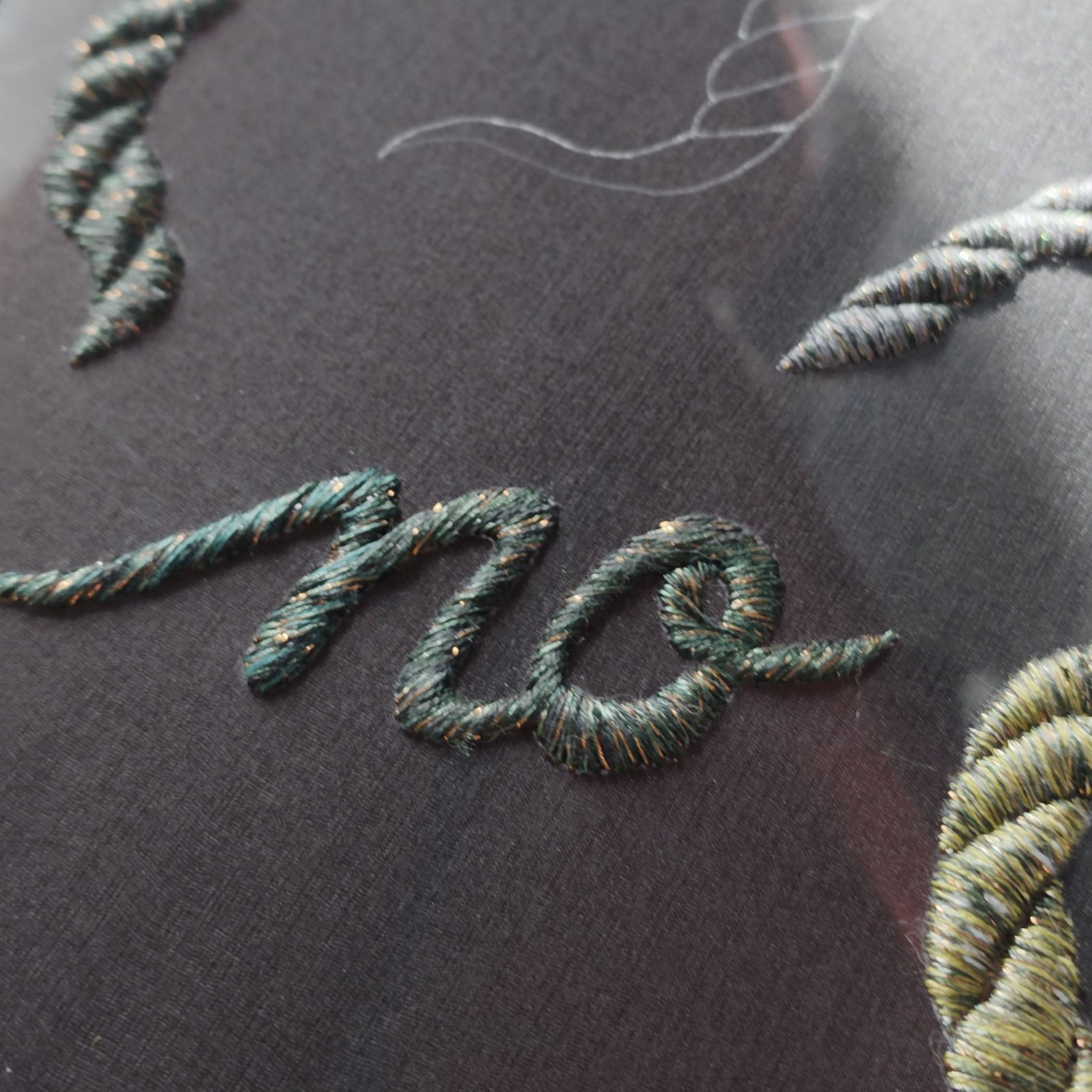 Close-up of embroidered lettering from Ksenia Semirova’s Power of No textile art series, stitched with green and metallic threads on sheer black fabric