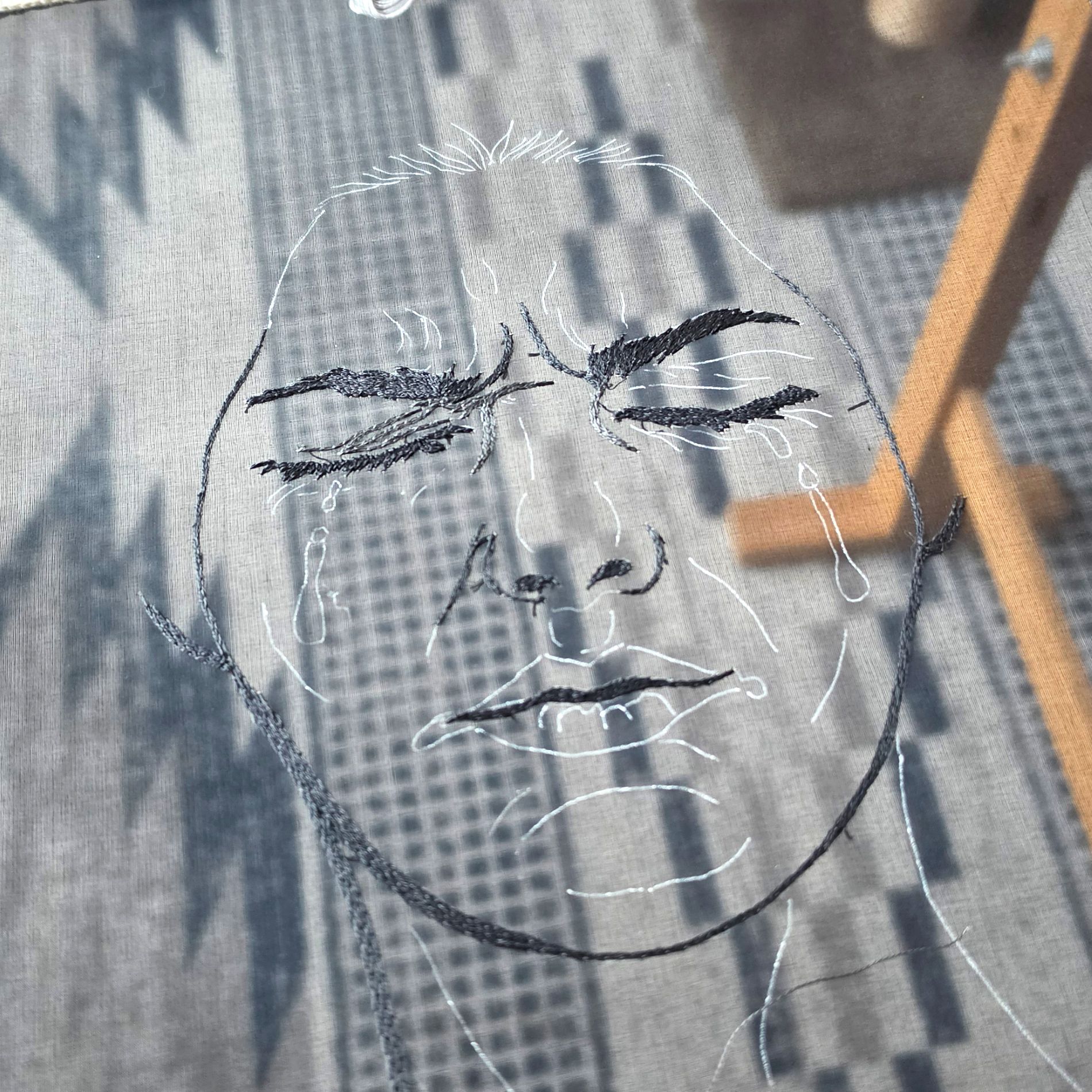Work in progress image of Sorrow from the Power of No series, showing the early hand embroidered crying face on sheer black fabric.