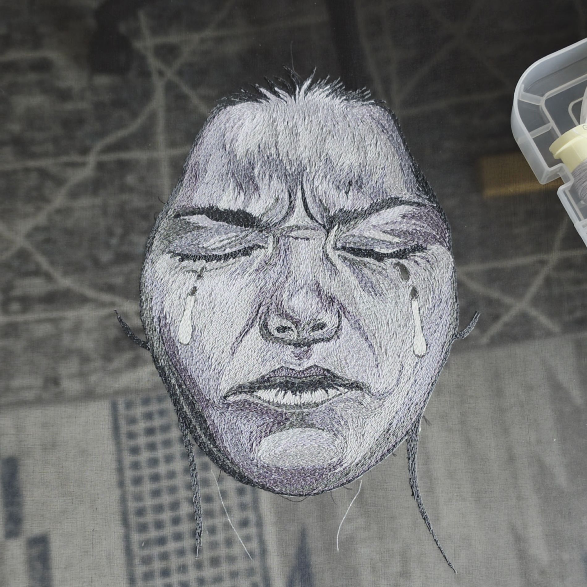 Close-up progress image of Sorrow from the Power of No series, showing a hand embroidered crying face on sheer black fabric