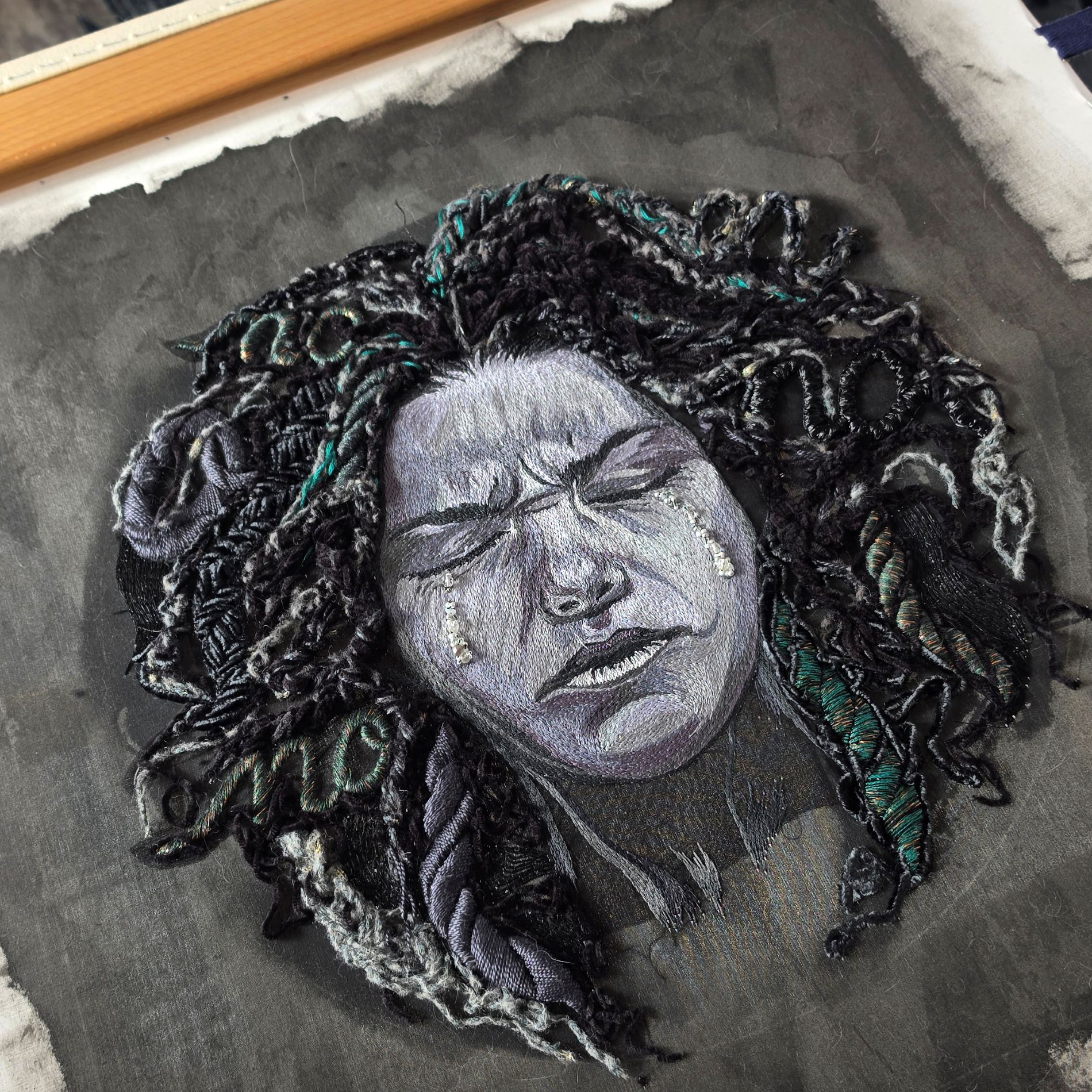 Hand embroidered textile wall art titled Sorrow from the Power of No series, featuring an expressive stitched portrait surrounded by layered black embroidery.