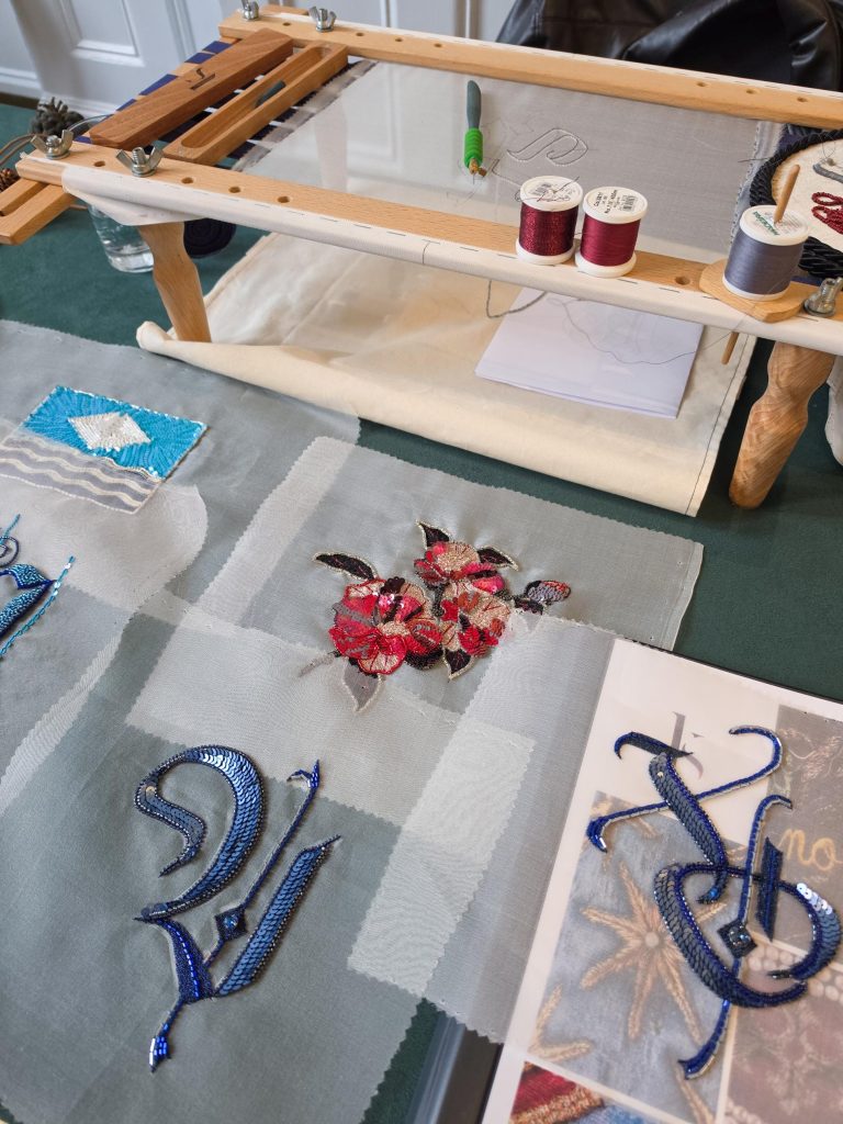 Floral and blue hand embroidered samples displayed beside a Luneville embroidery frame.